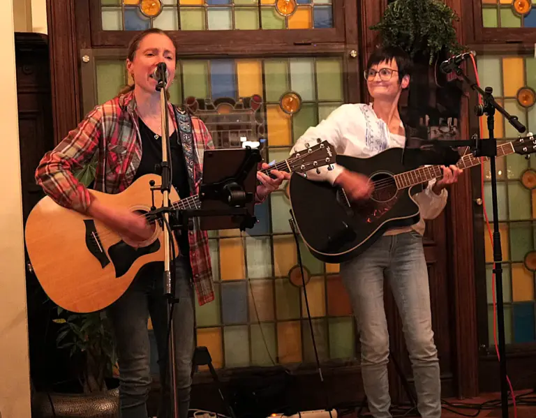 Singer Songwriterin Isolde singt mit Akustikgitarre live mit ihrer Musikerkollegin vom Akustikduo ProMrs auf einer Bühne.